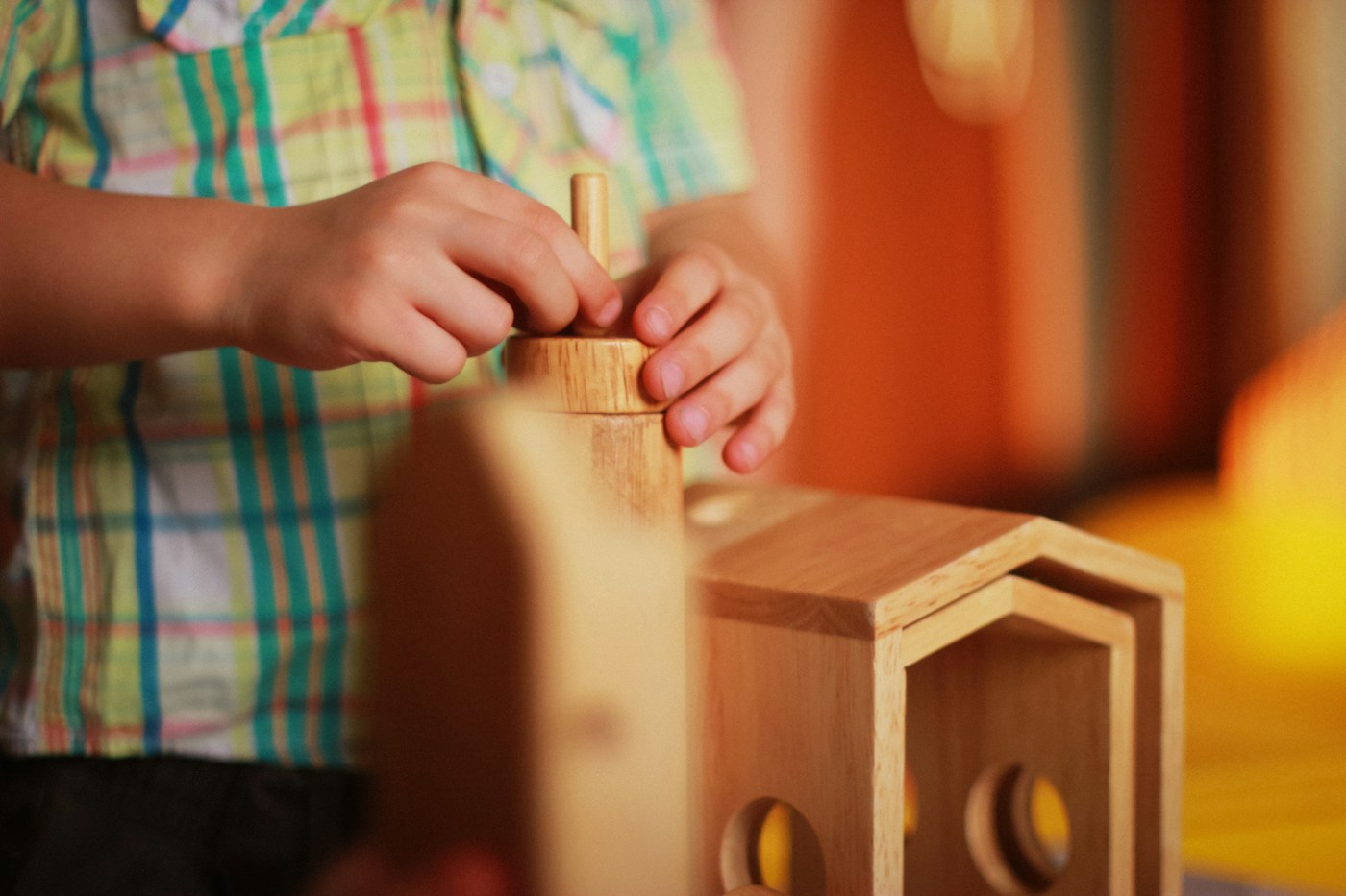 A child's hands fitting a wooden peg into a stacking toy